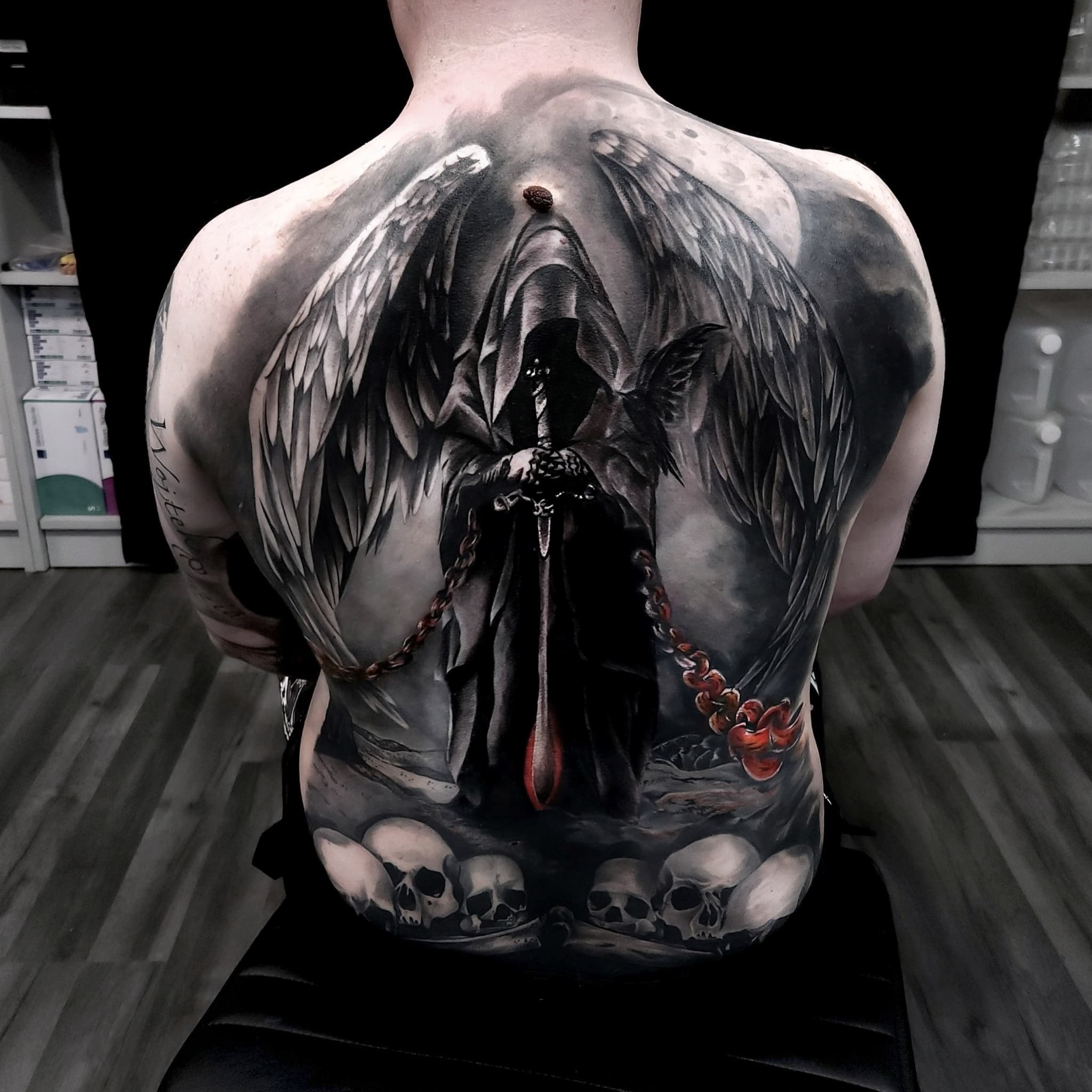 Realistyczny tatuaz mrocznego aniola z mieczem czaszkami i skrzydlami na calych plecach