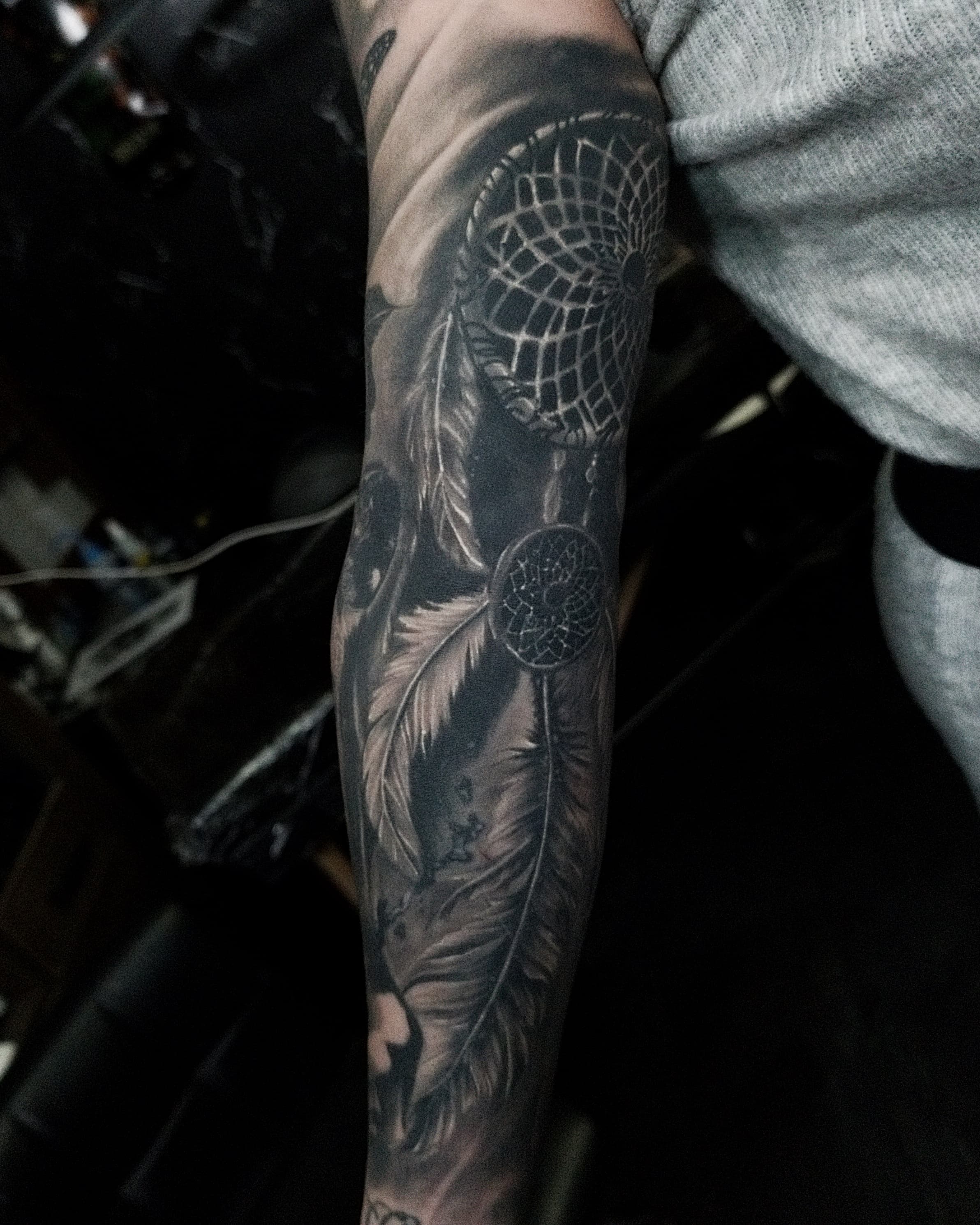 Czarno-szary realistyczny tatuaz łapacza snów z piórami na całym przedramieniu
