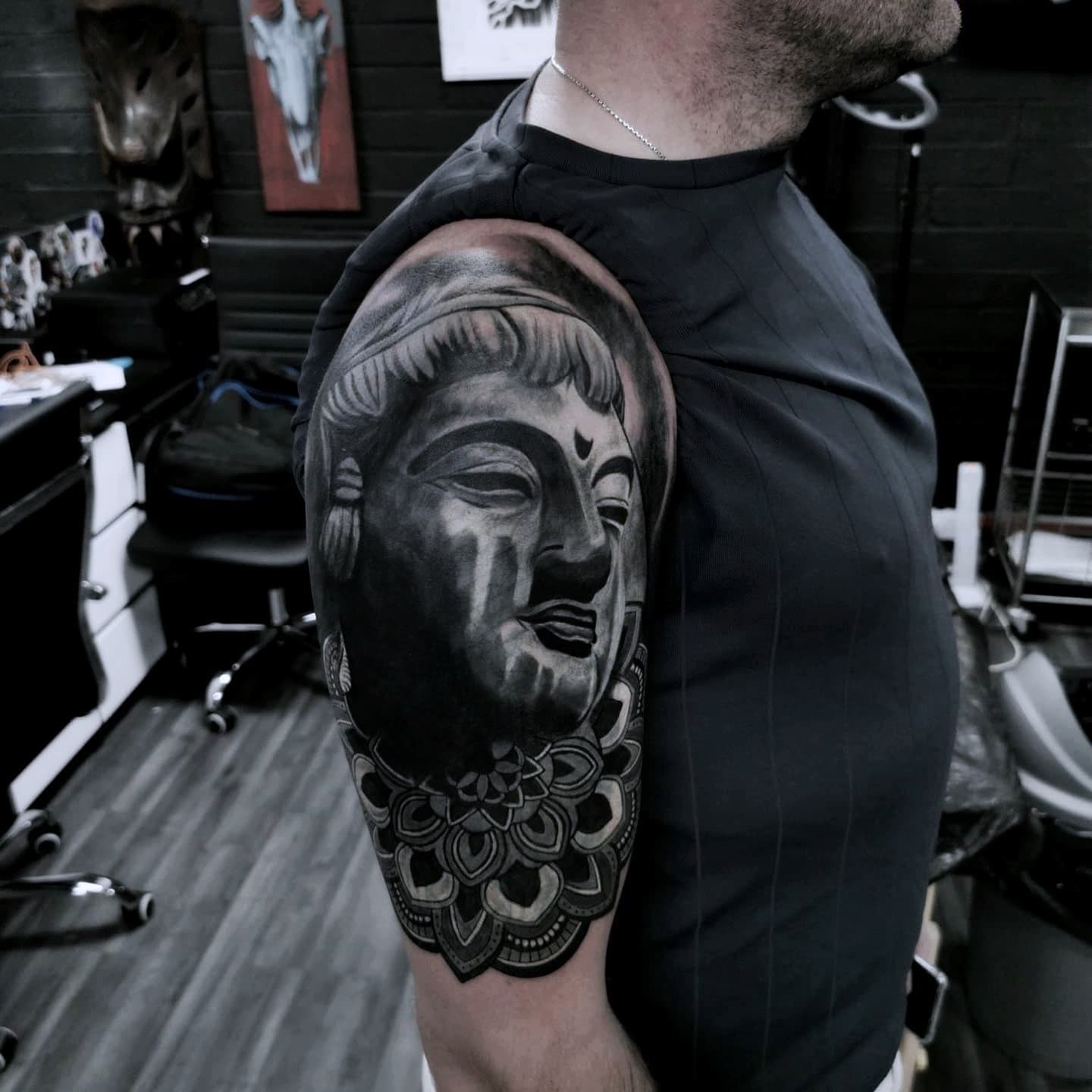 Realistyczny tatuaz twarzy Buddy z mandala na ramieniu mezczyzny w czerni i szarosci