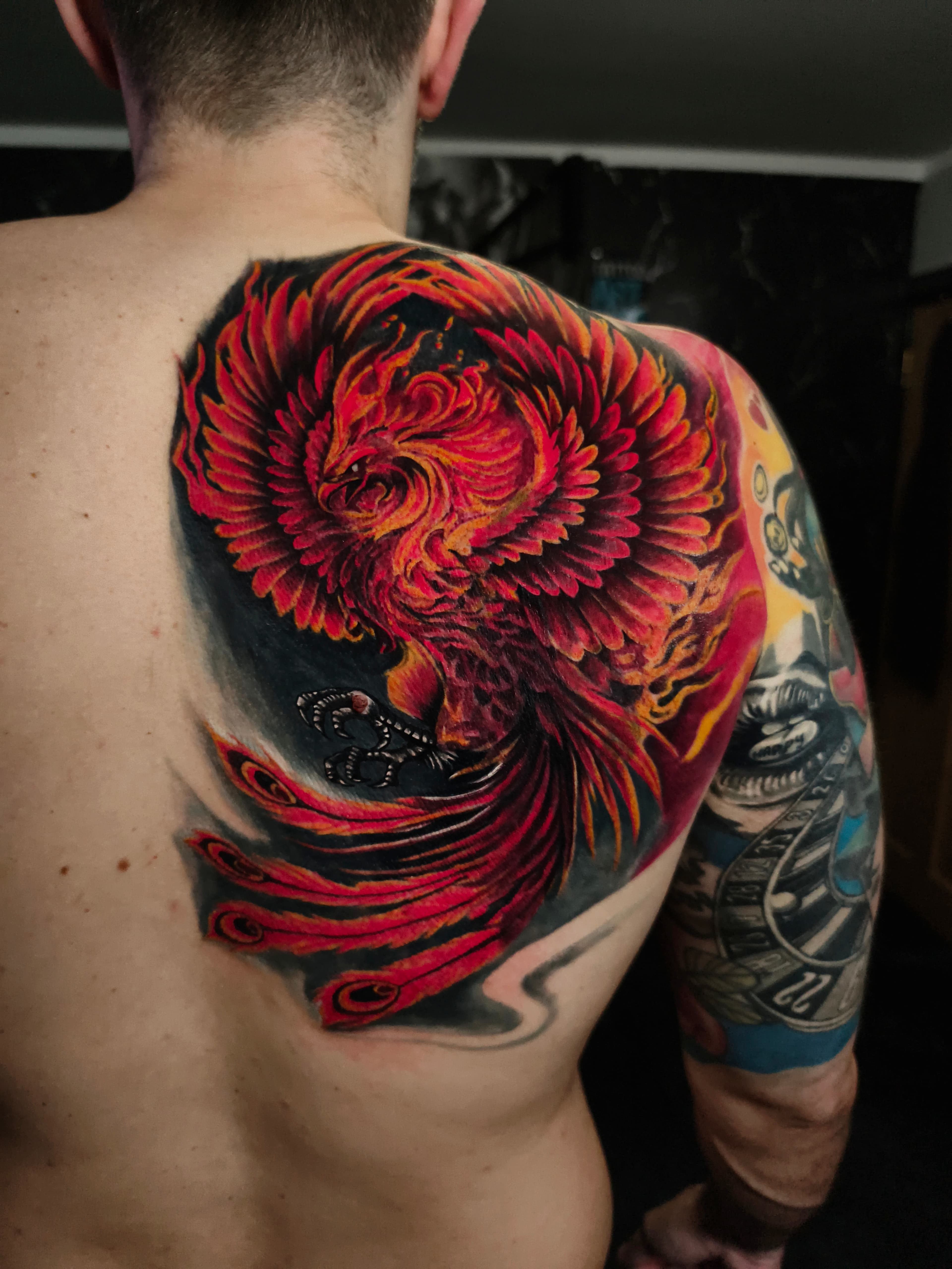 Kolorowy realistyczny tatuaz feniksa na plecach i ramieniu z ognistymi skrzydłami w czerwieni