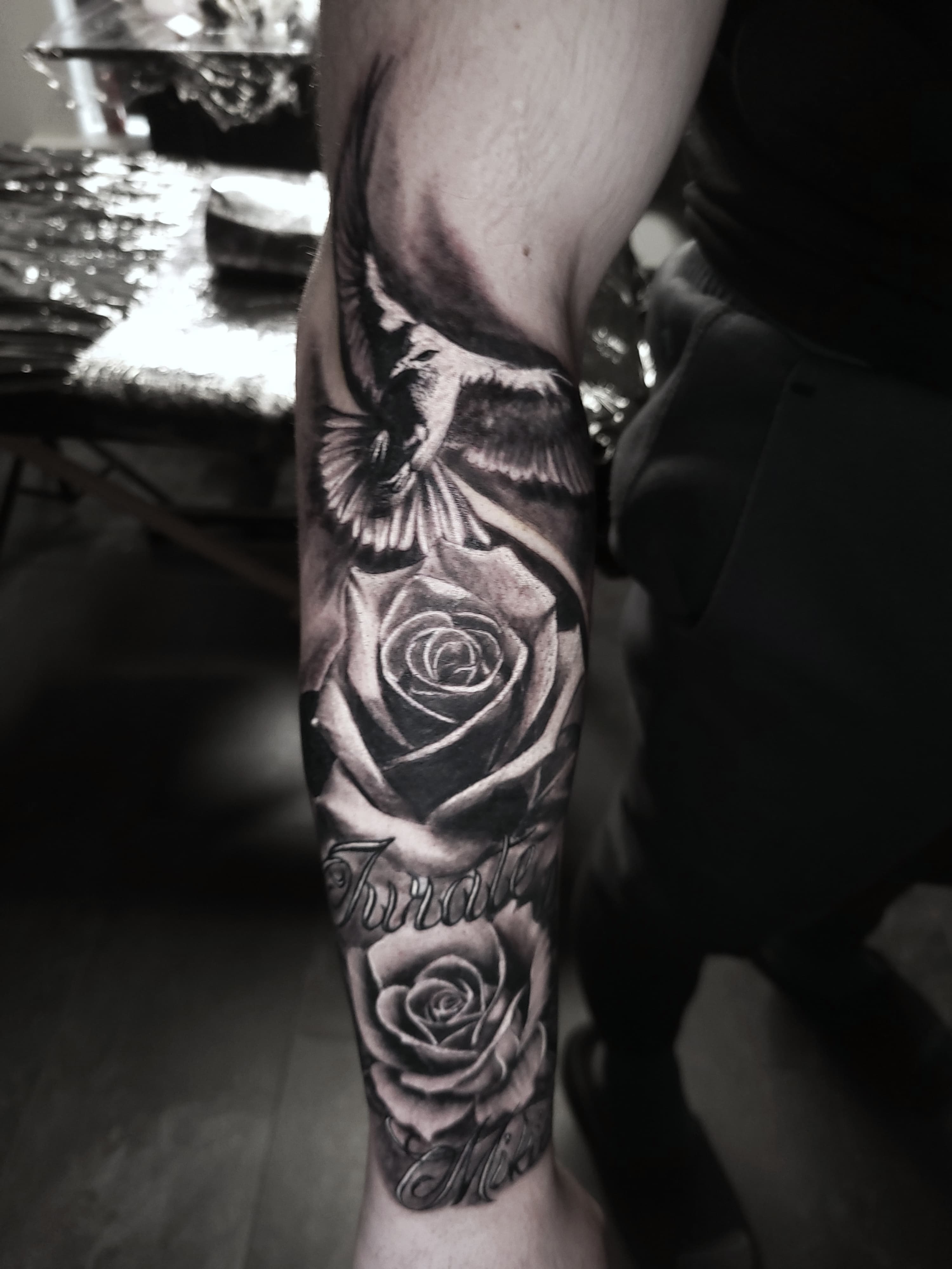 Realistyczny tatuaz gołębia w locie z różami i napisem na przedramieniu czarno-szary