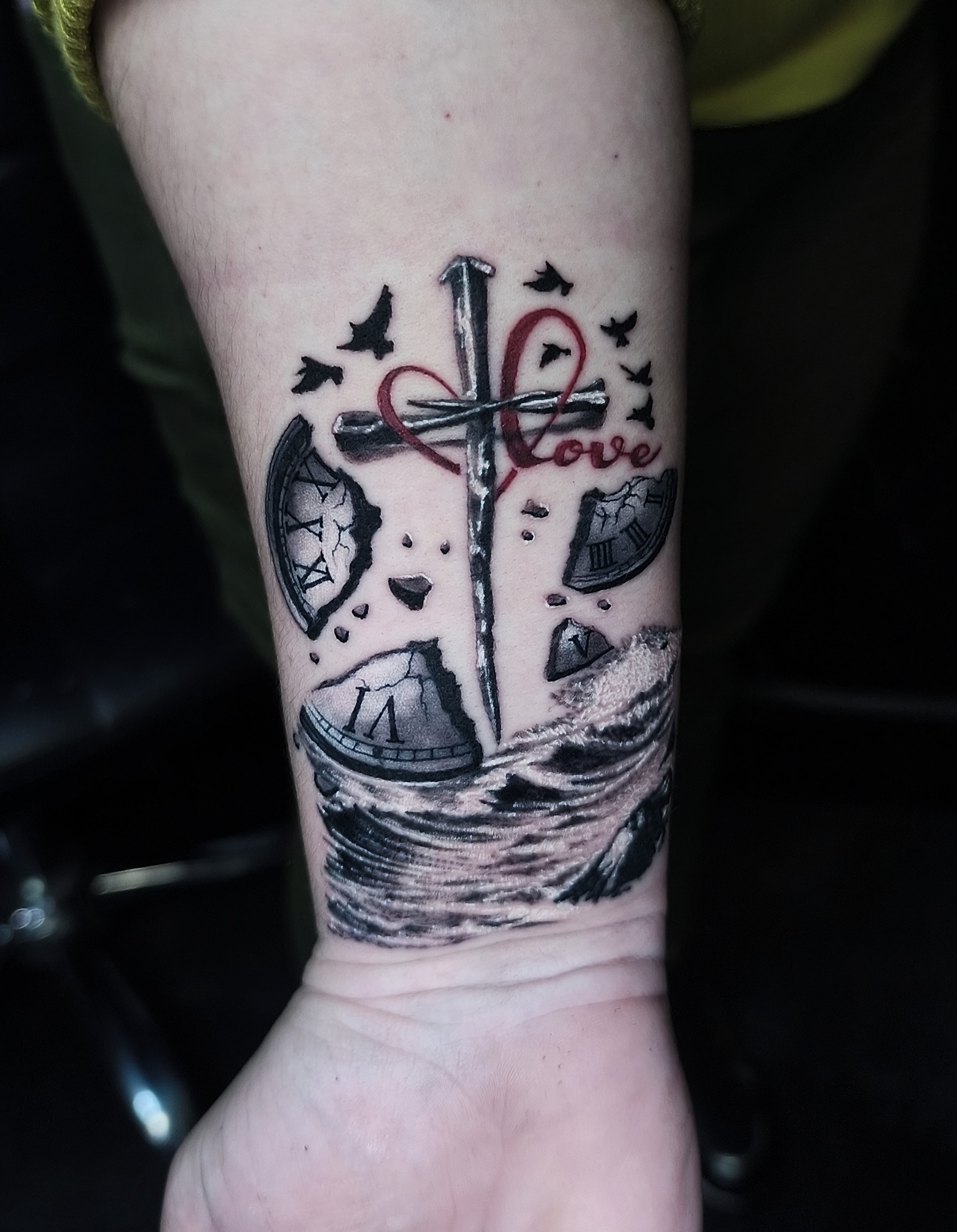 Czarno-bialy tatuaz na nadgarstku z krzyżem, rozbitym zegarem, falami morskimi i ptakami