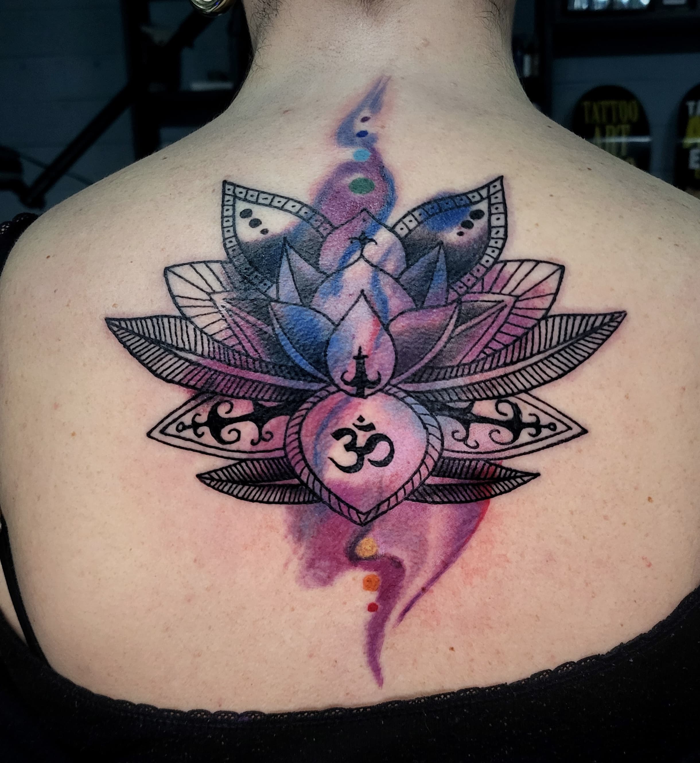 Kolorowy tatuaz kwiatu lotosu z symbolem Om na plecach z akcentami akwarelowymi