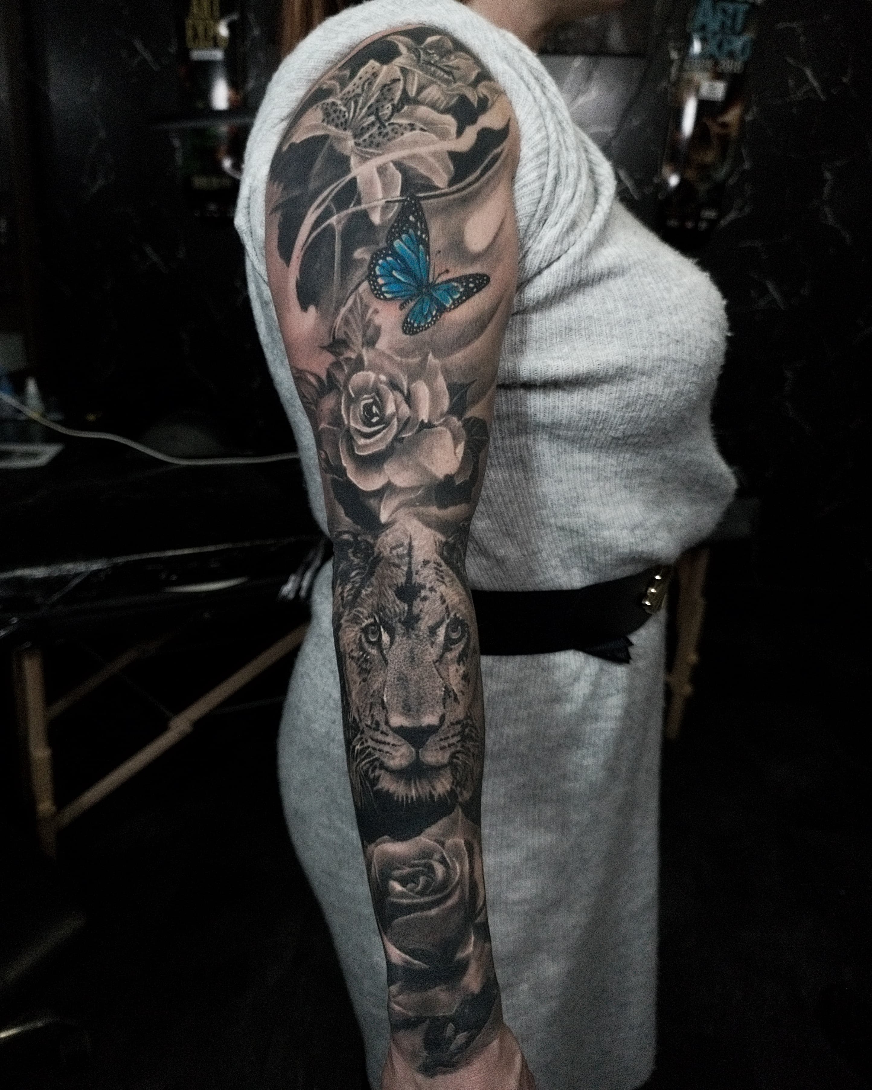 Czarno-szary rękaw tatuazu z lwicą, różami i niebieskim motylem w realistycznym stylu