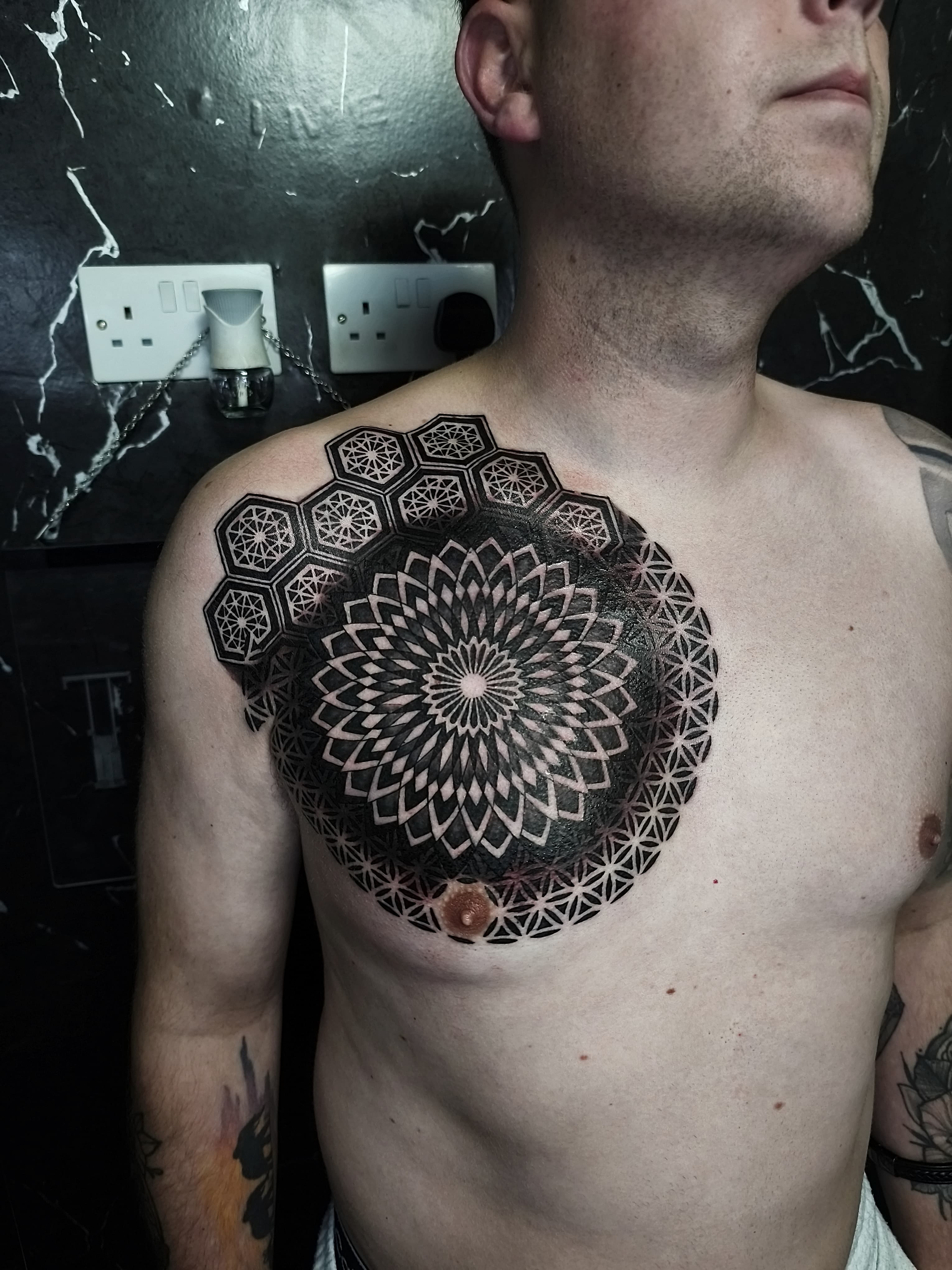 Czarno-bialy geometryczny tatuaz mandali na klatce piersiowej z heksagonami i kwiatem życia
