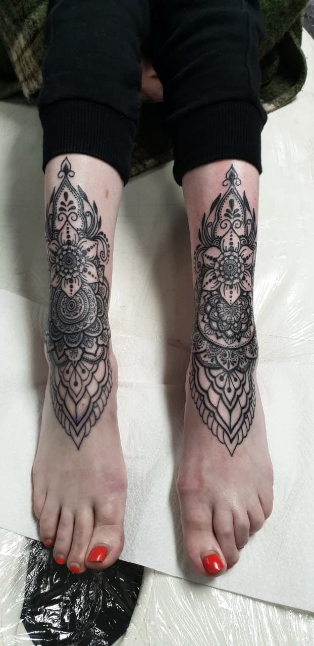 Symetryczne ornamentalne tatuaze mandali w stylu linework na obu lydkach kobiety