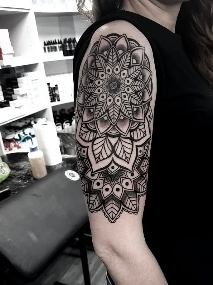 Czarno-bialy tatuaz mandali na ramieniu z symetrycznymi wzorami kwiatowymi i listkami