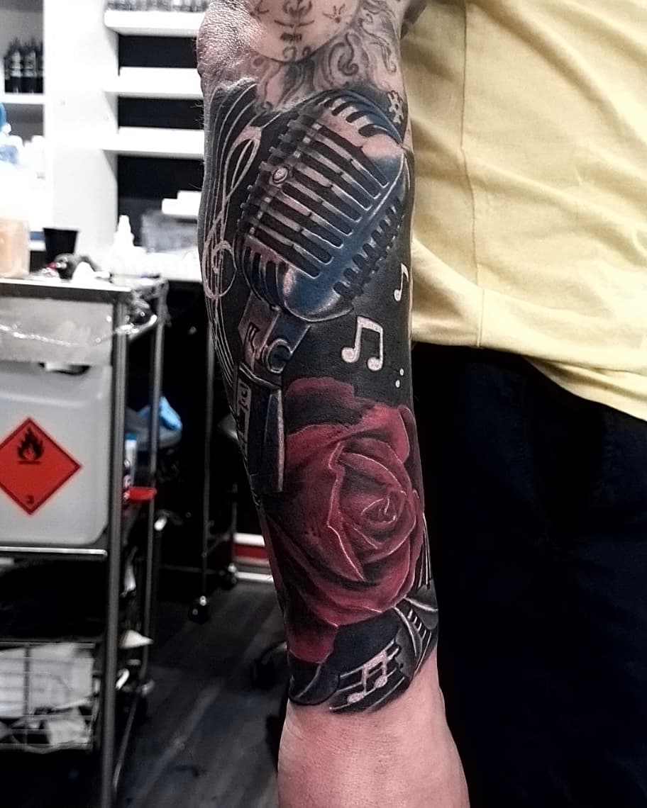 Realistyczny tatuaz na przedramieniu z retro mikrofonem, różą i nutami muzycznymi