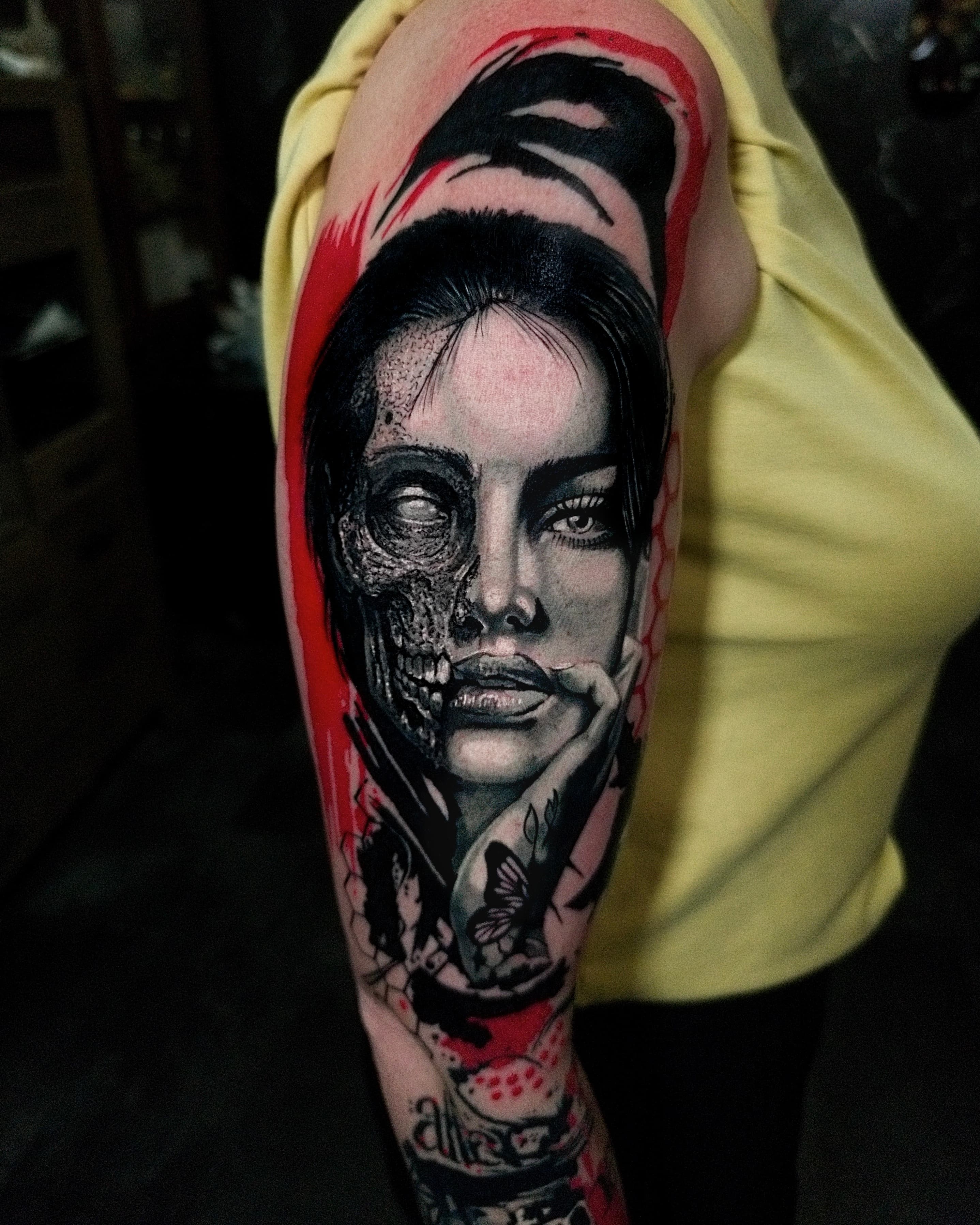 Realistyczny tatuaz kobiety z pół czaszka i czerwonymi akcentami zblizenie na ramieniu