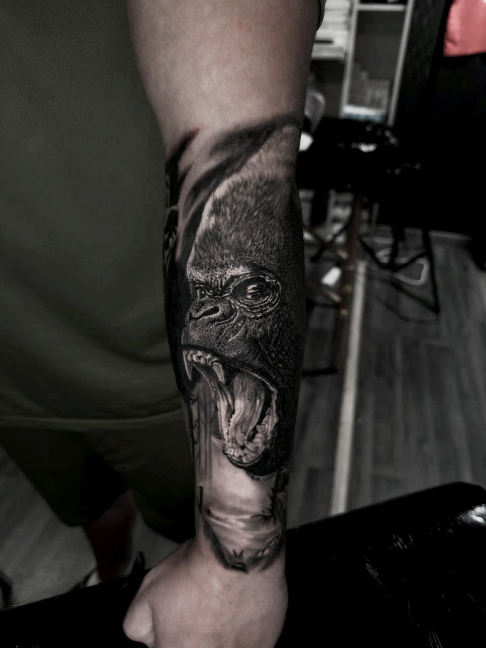 Realistyczny czarno-bialy tatuaz ryczącego goryla na przedramieniu z detalami futra i zębów