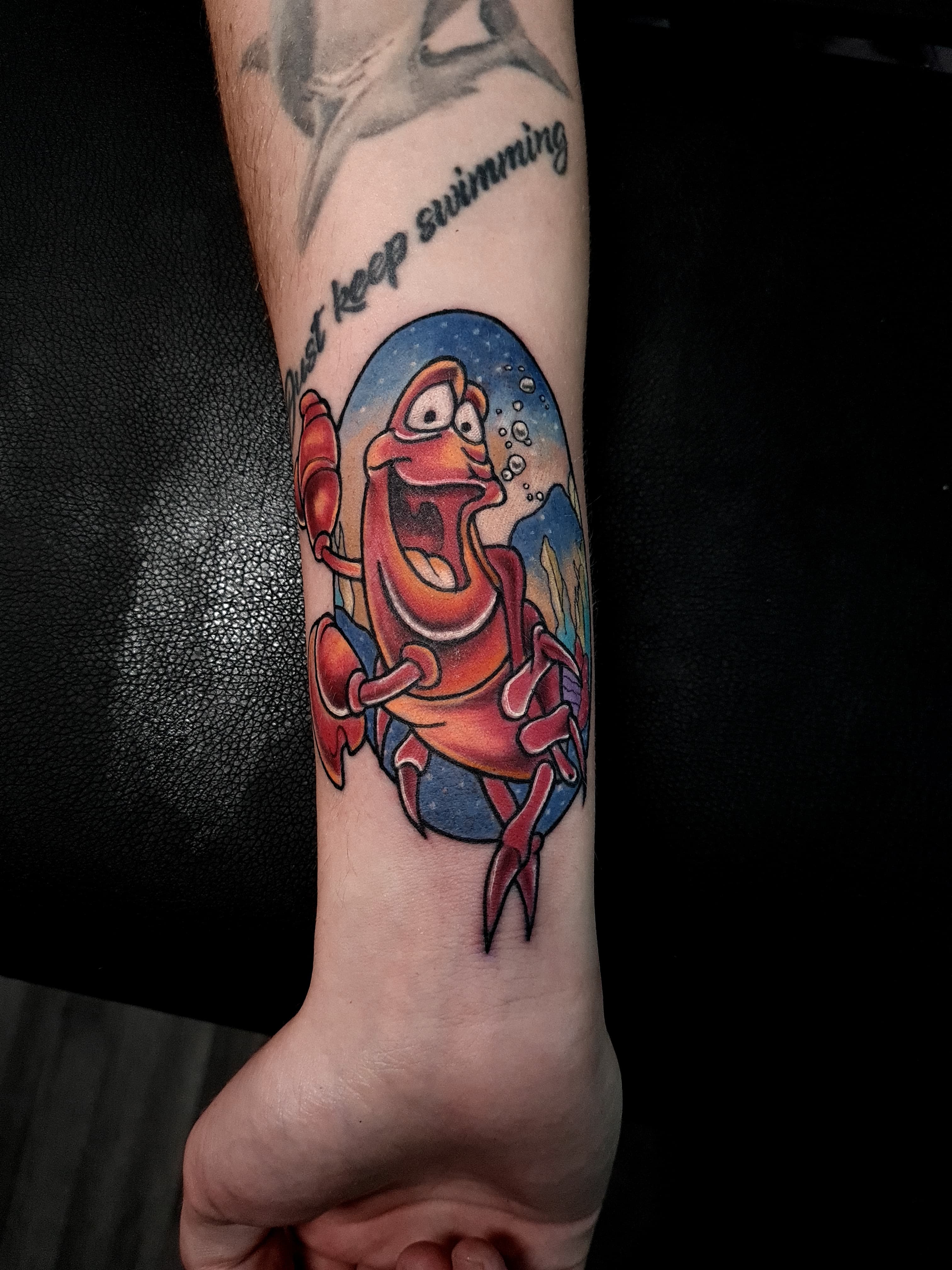 Kolorowy tatuaz kraba Sebastiana z Malej Syrenki na przedramieniu w stylu cartoon