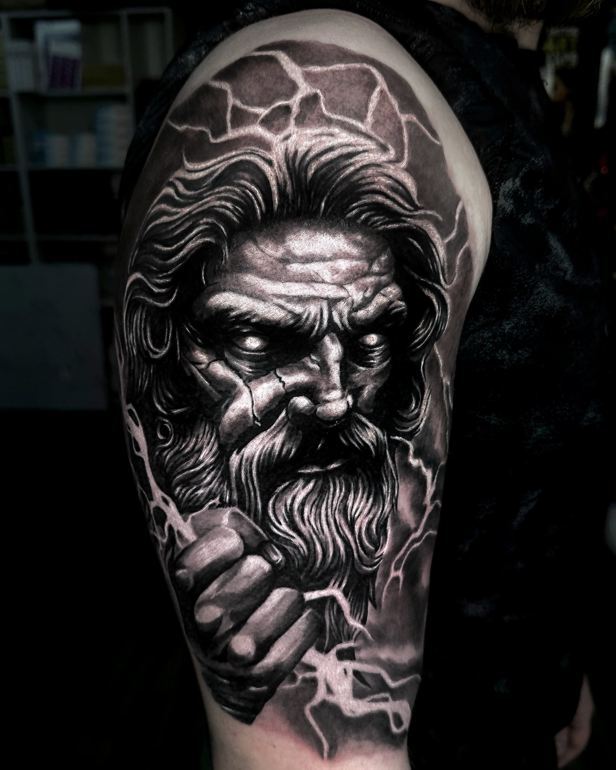 Realistyczny tatuaz Zeusa z blyskawicami i broda w odcieniach szarosci na ramieniu
